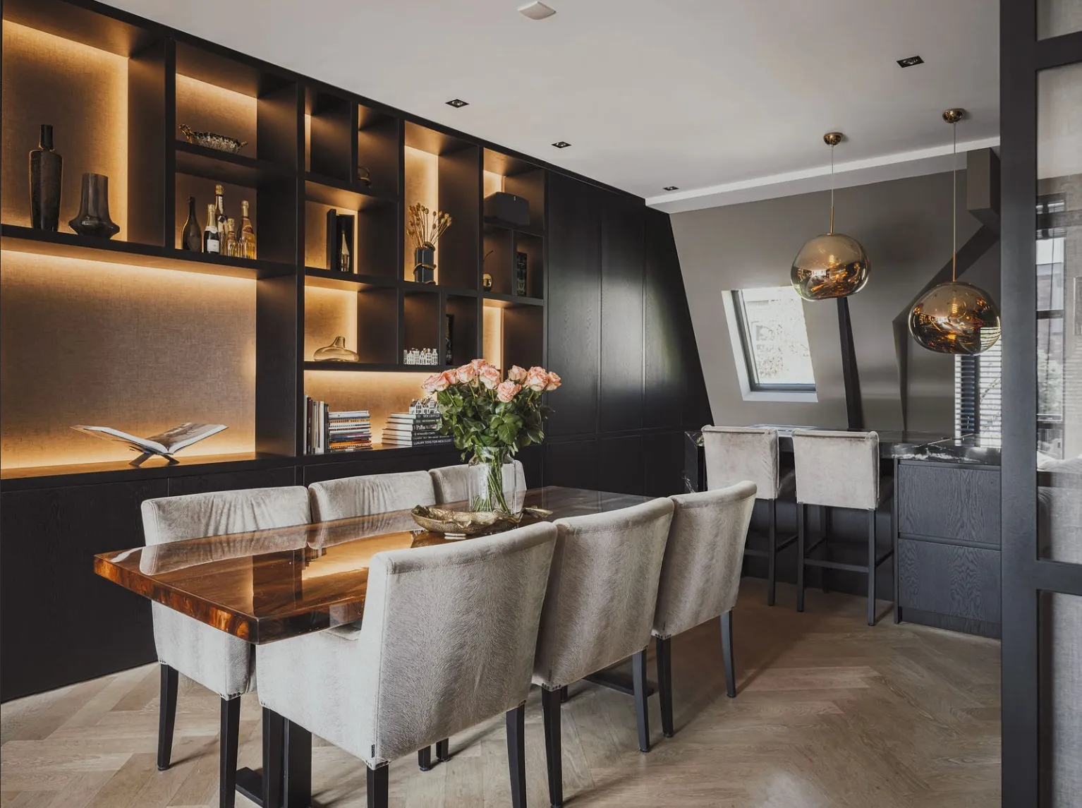 Eettafel voor de showkast met zicht op het keukeneiland en de gouden hanglampen