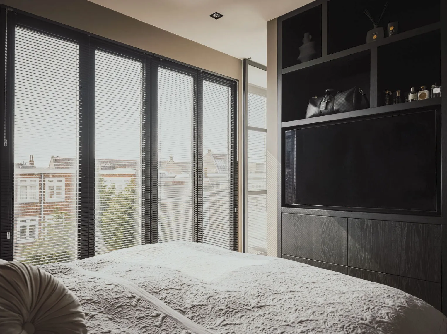 Zwart eiken tv-meubel met open vakken in de slaapkamer, met zicht over de daken van Amsterdam-Zuid