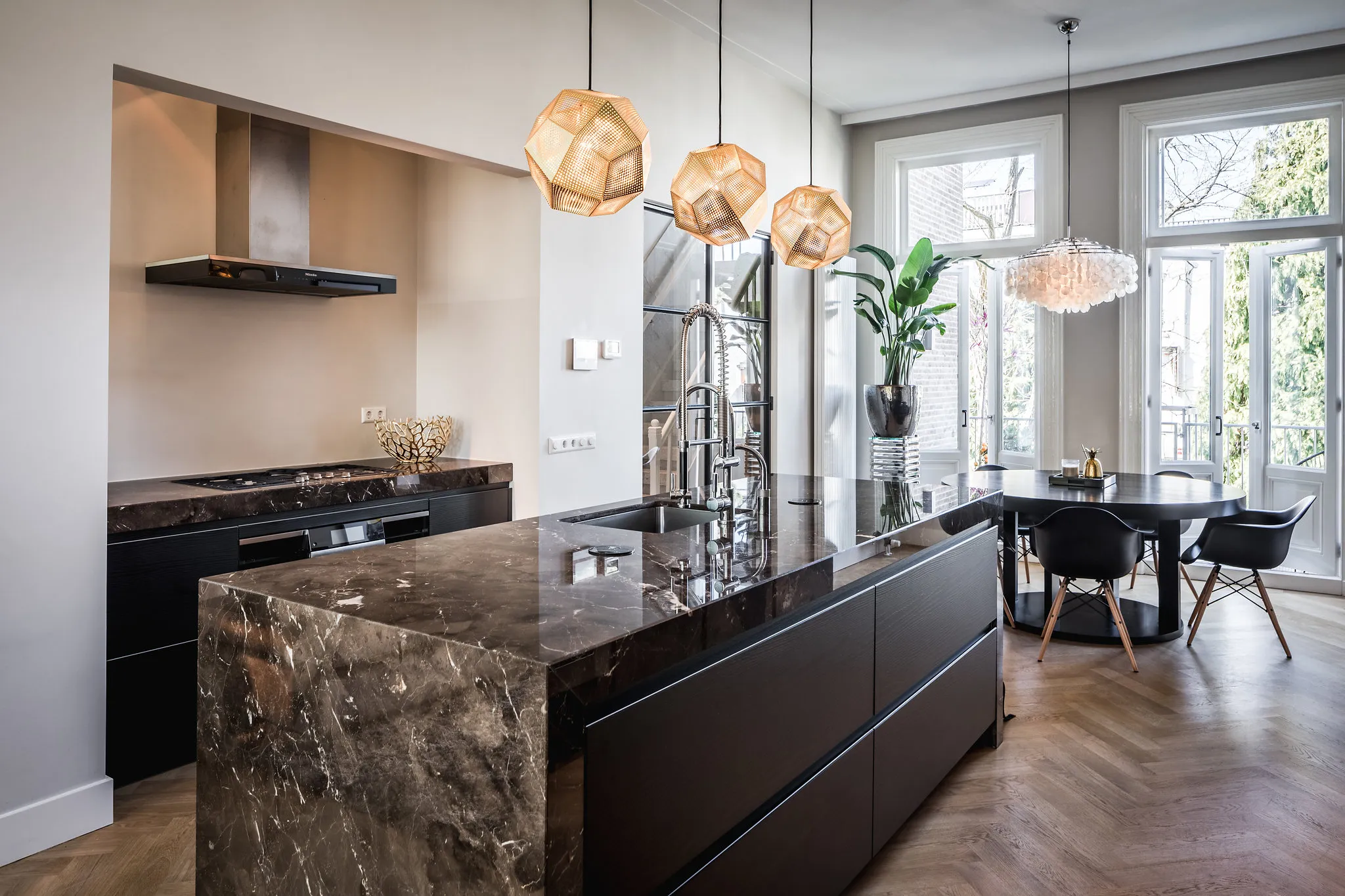 Keuken met natuurstenen eiland, gaskookplaat en ronde zwarte eettafel bij de openslaande deuren