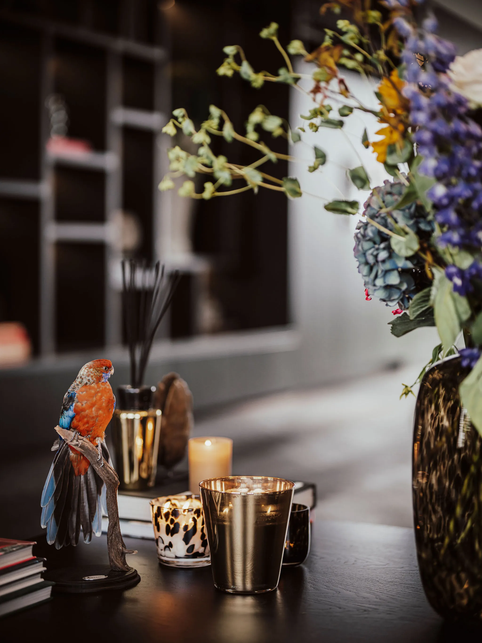 Styling op het zwart eiken dressoir met een opgezette vogel op tak, goudkleurige waxinelichthouders en een boeket