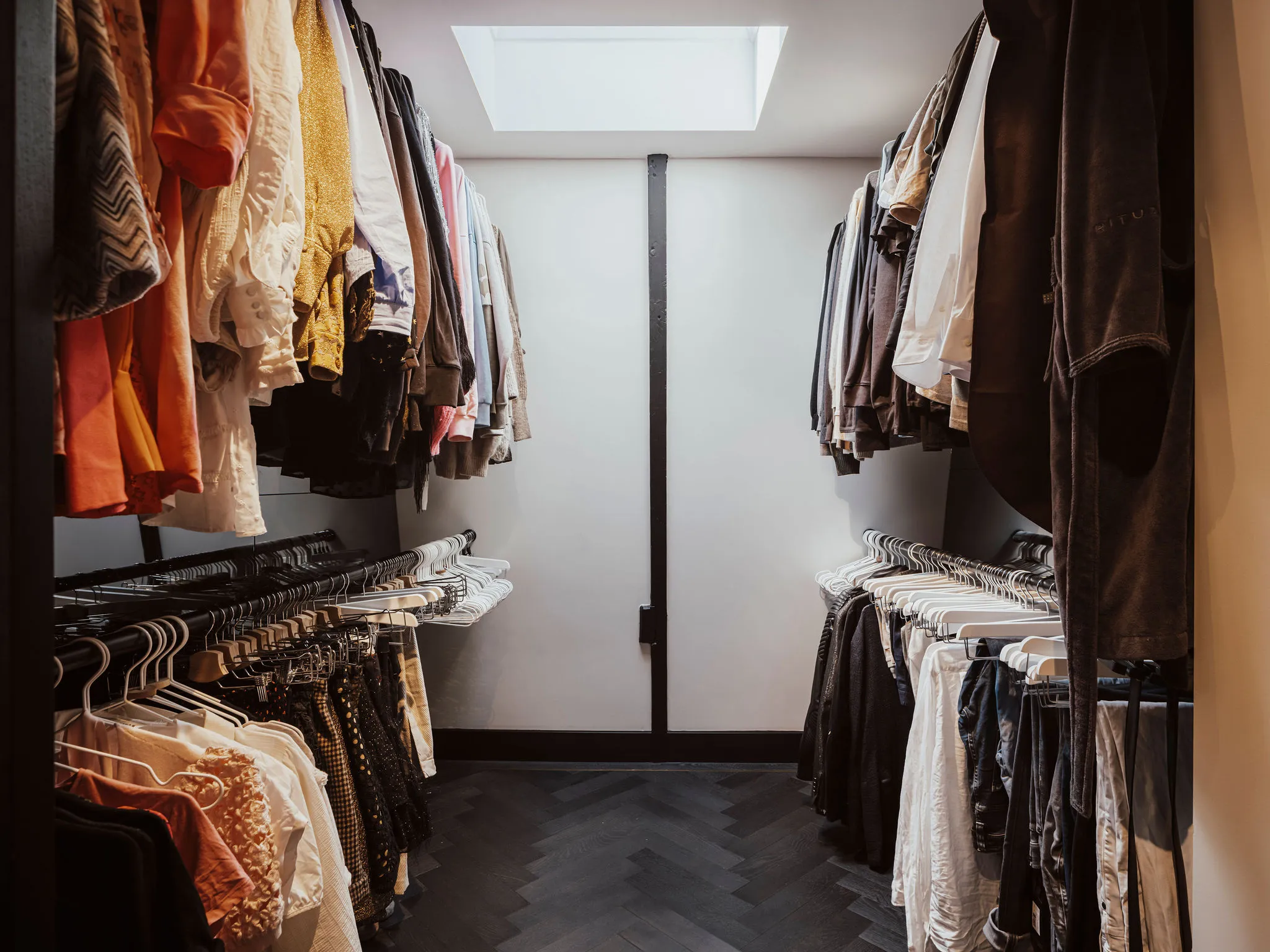 Walk-in closet achter de kastenwand met hangroedes aan beide zijden en donkere visgraatvloer