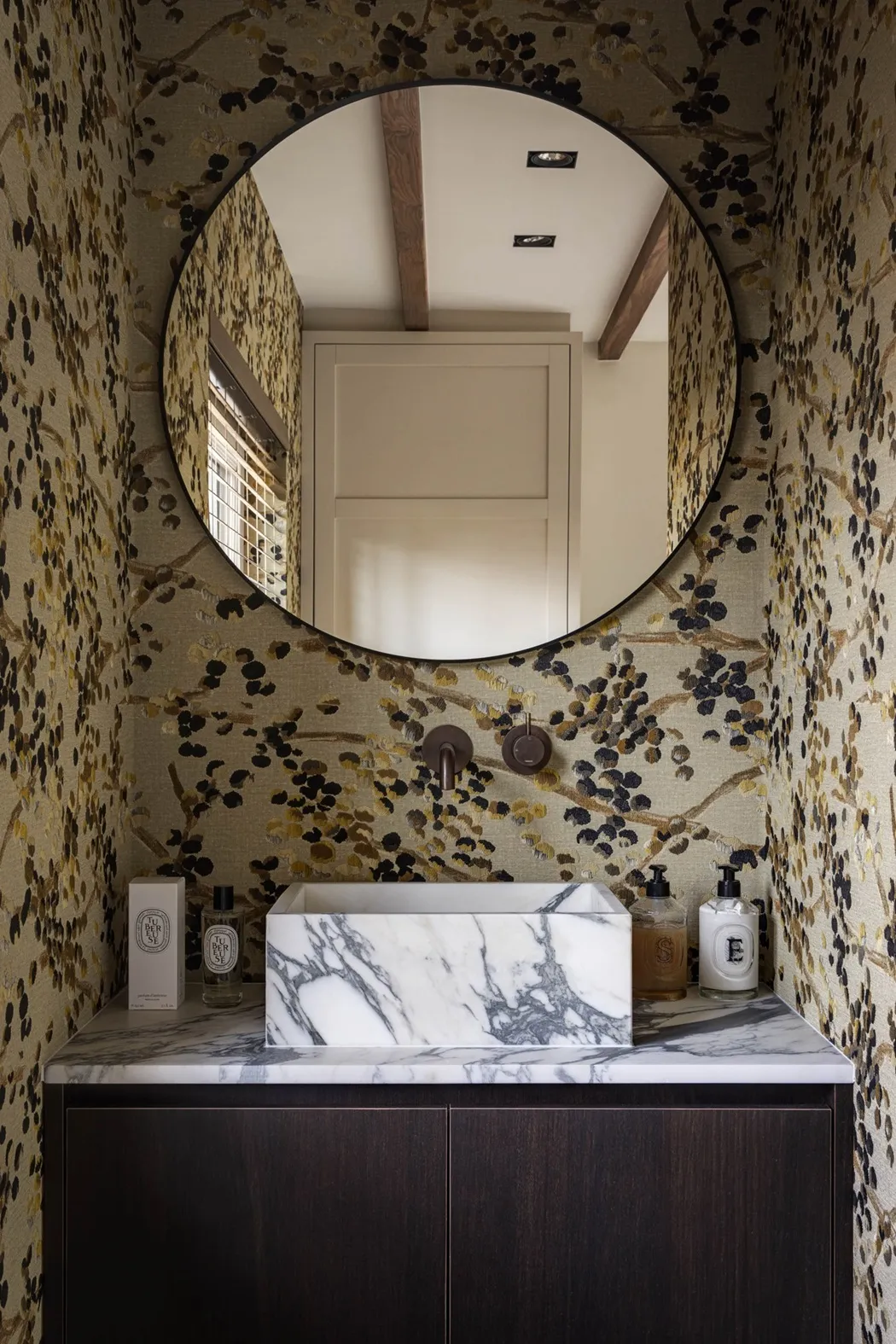 Toiletmeubel van donker eikenhout met wit marmeren blad en opzetwasbak, wandkraan in brons en ronde spiegel tegen botanisch behang