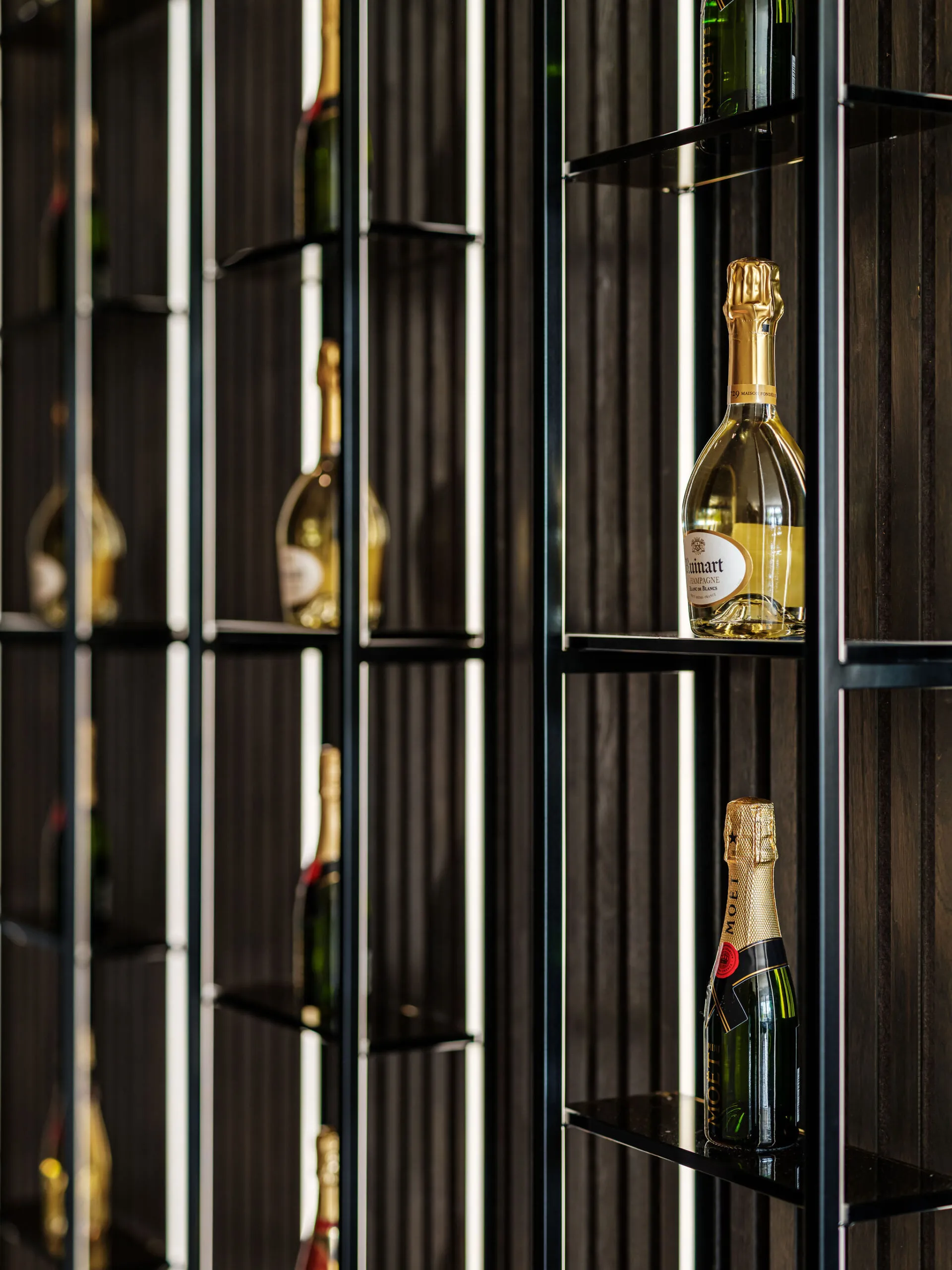 Verlichte vitrinekast met glazen schappen en champagneflessen achter zwart lattenwerk
