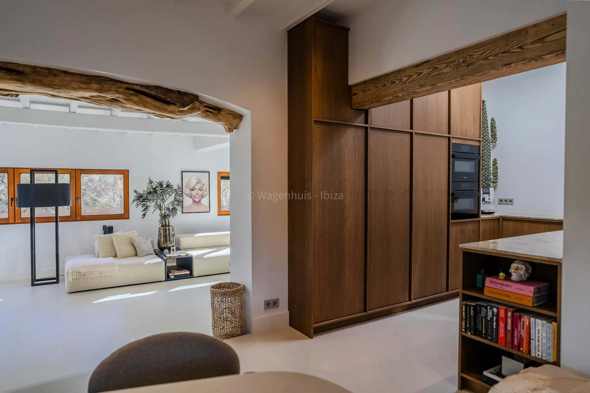Doorkijk vanuit de eetkamer naar de eikenhouten kastenwand met ingebouwde apparatuur, onder een oude houten balk